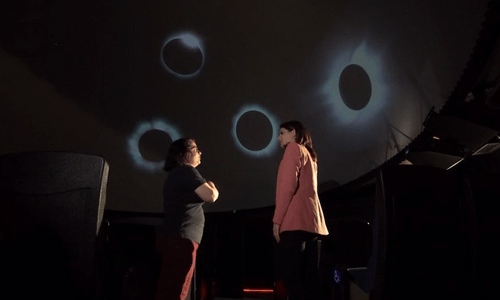 2 women in planetarium with eclipse images