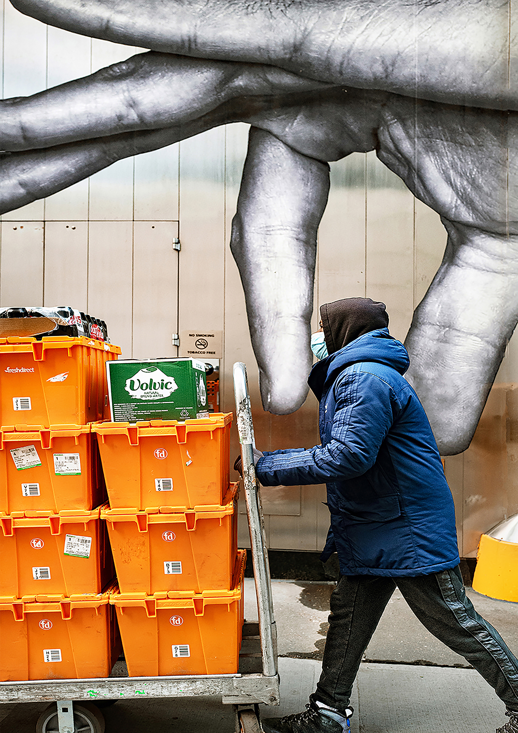 photo of person pushing cart of orange crates with giant hand above