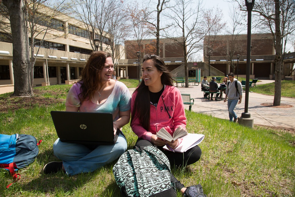 2 female students with laptop and book in quad