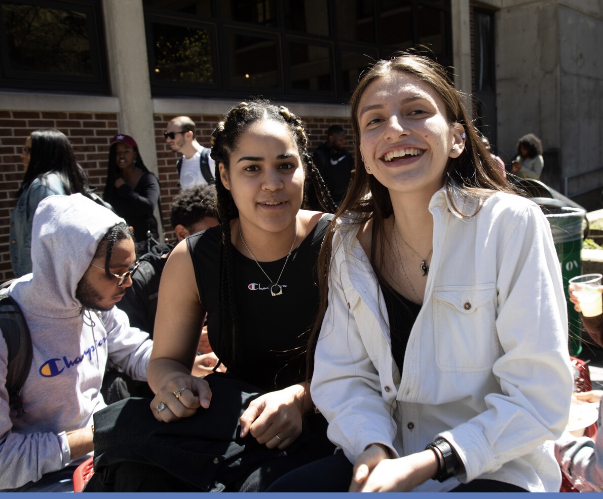 cropped version of 2 students outside in foreground with others around them