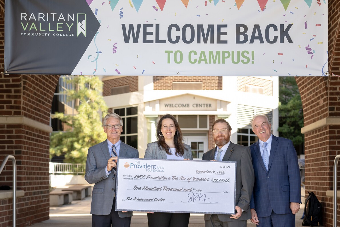 welcome back sign and four people with giant check