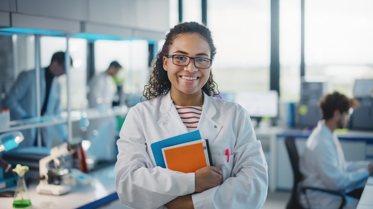 young female scientist in white lab coat holding textbooks