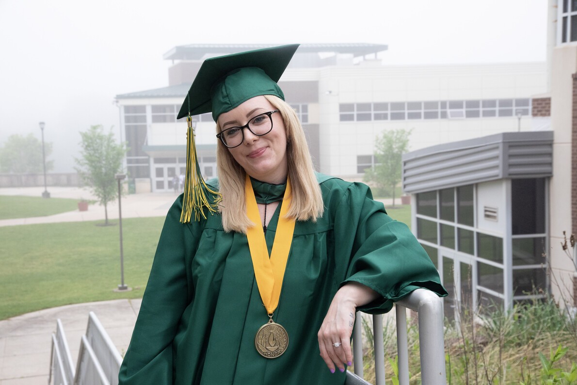 blonde graduate wearing glasses standing outside