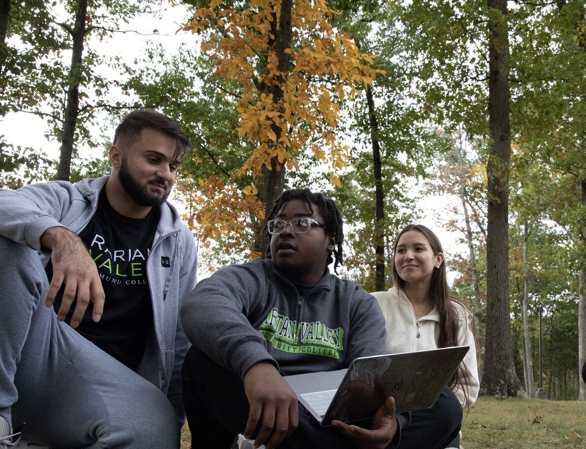 three students outside with middle student holding laptop