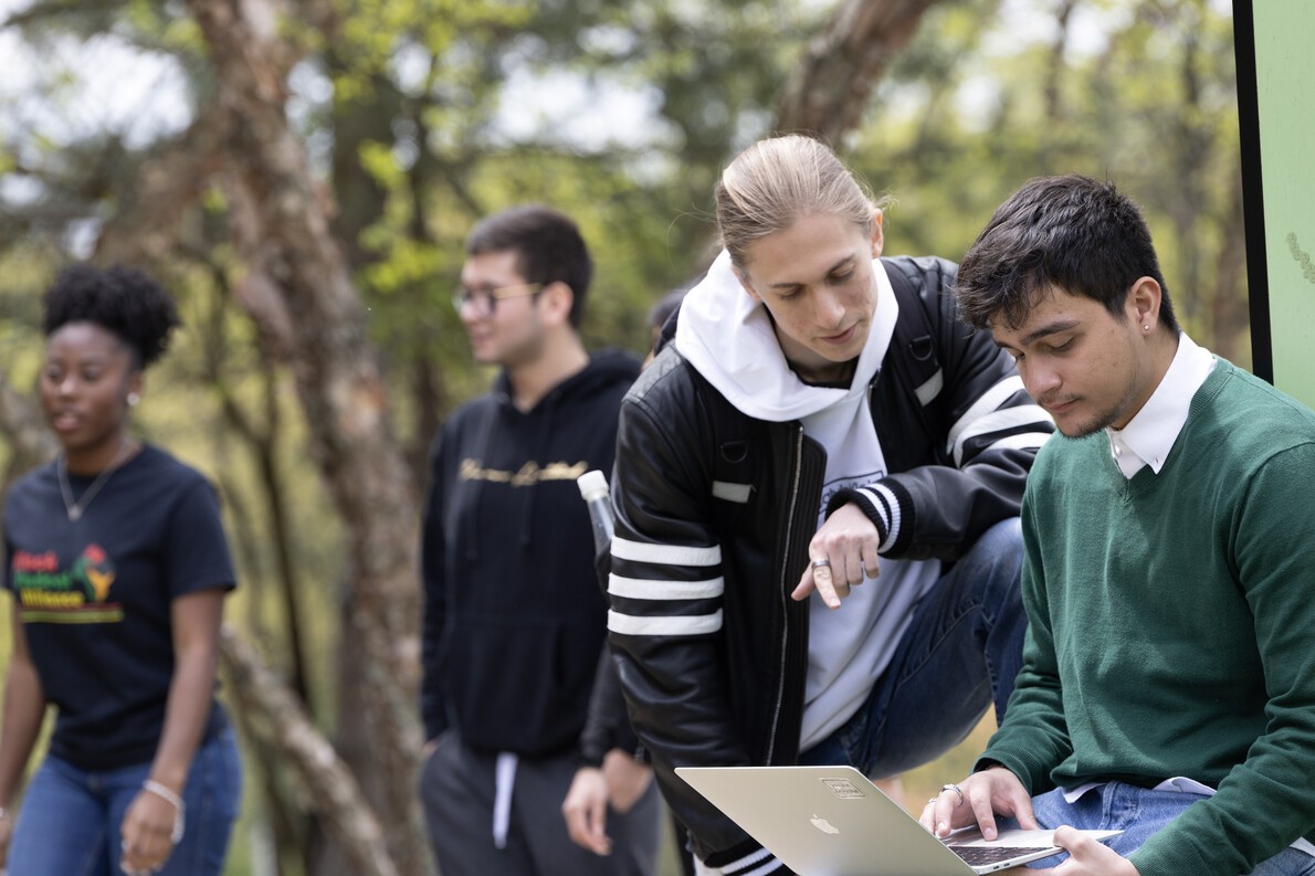 four students outside with one holding laptop