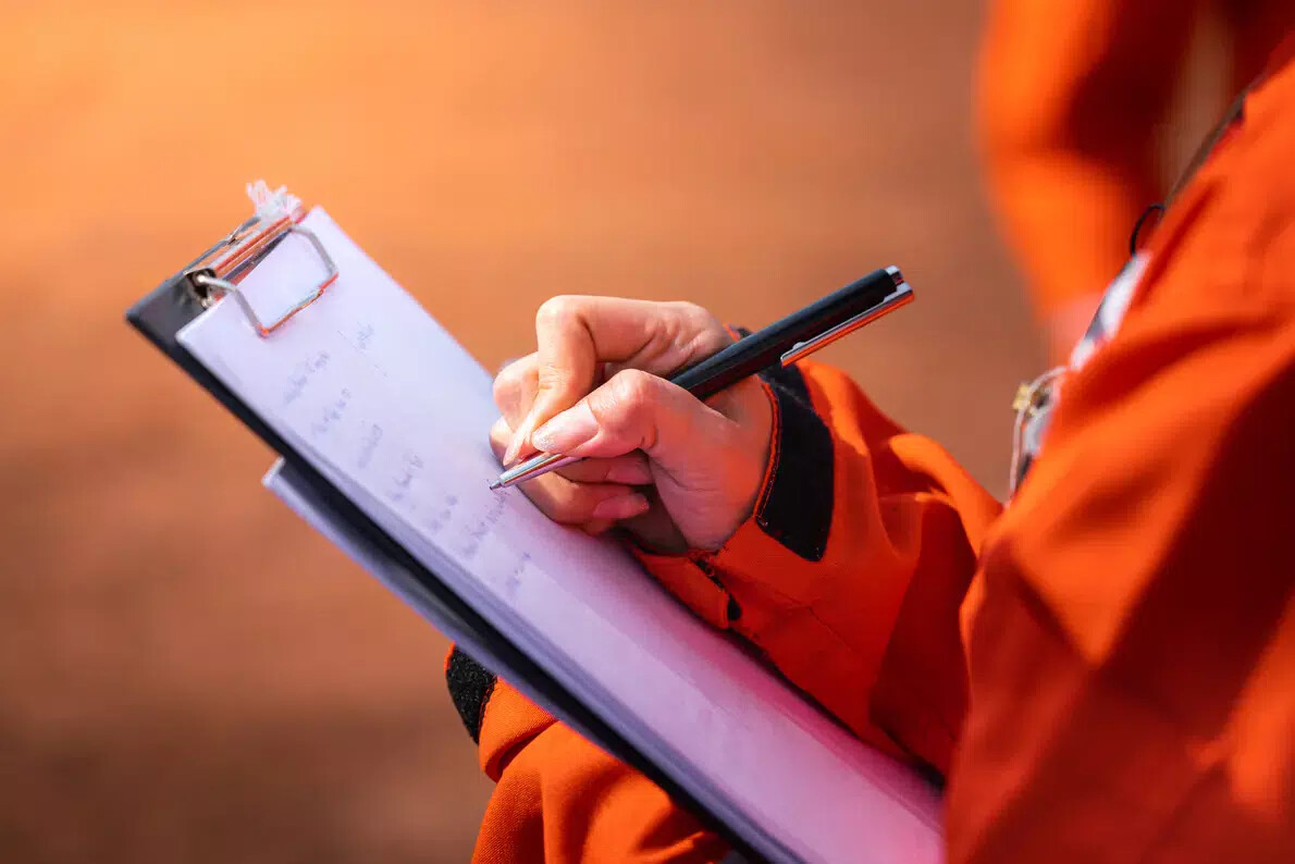 worker in orange suit writing notes on pad