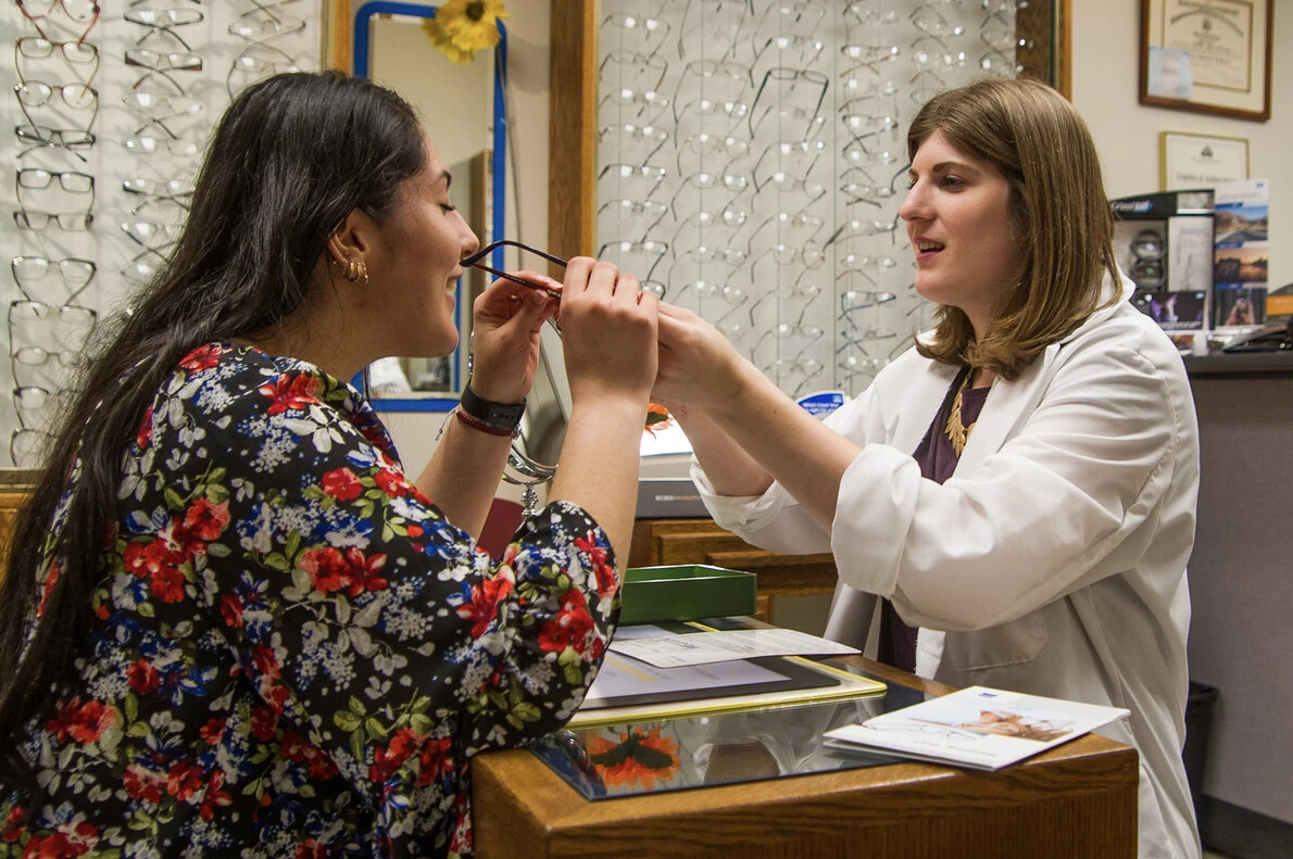 woman helping a another woman try on glasses
