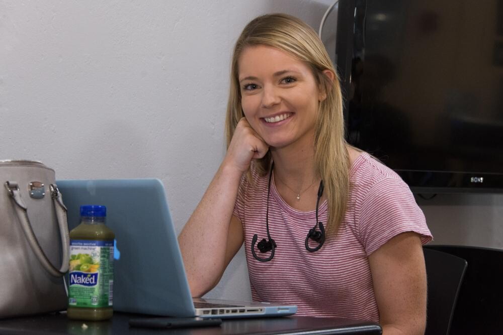 smiling girl with blonde hair wearing pink top using laptop