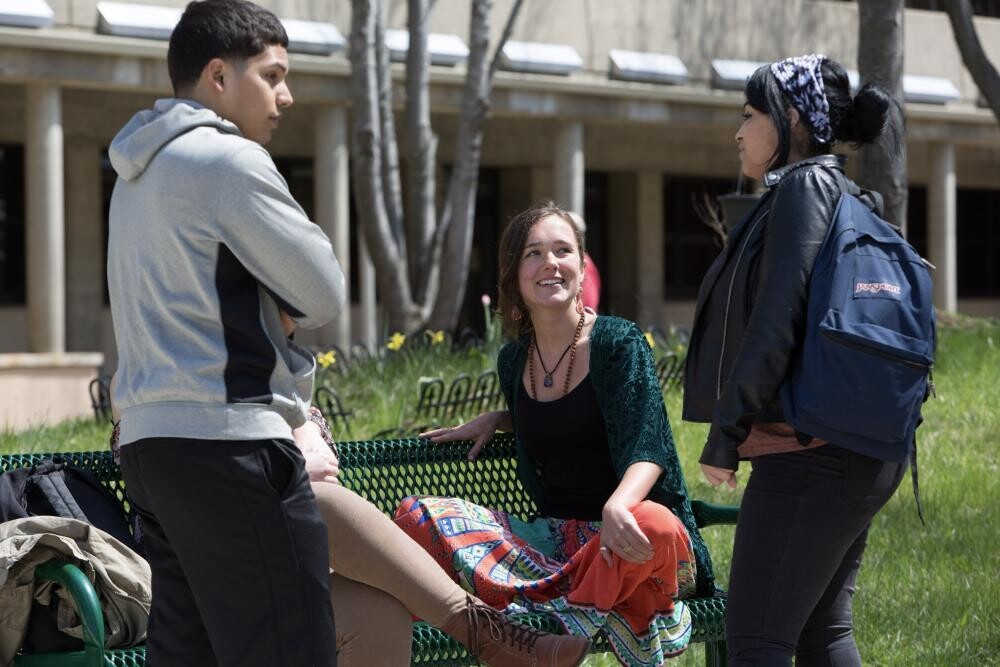 3 students outside on campus with one seated
