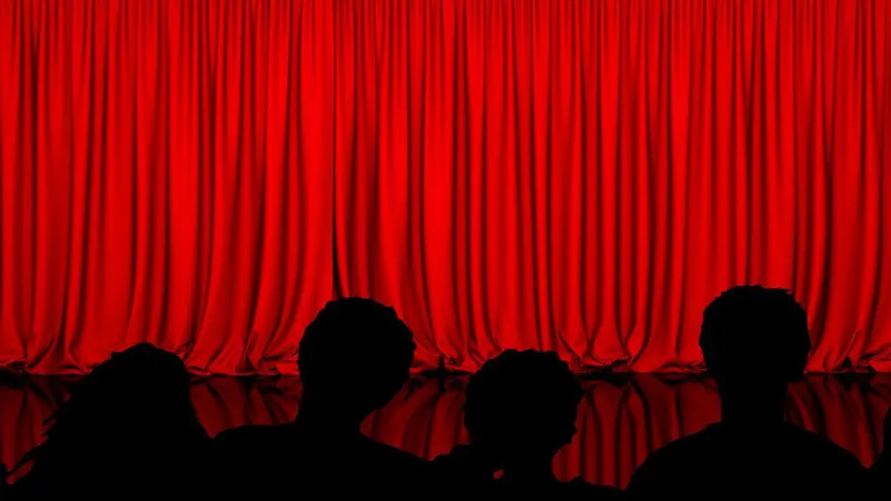 red curtain and backs of audience members heads