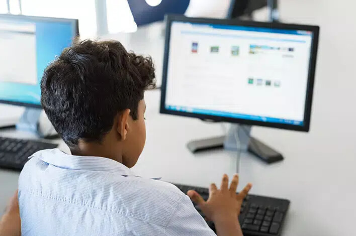 back of boy wearing light blue shirt at computer