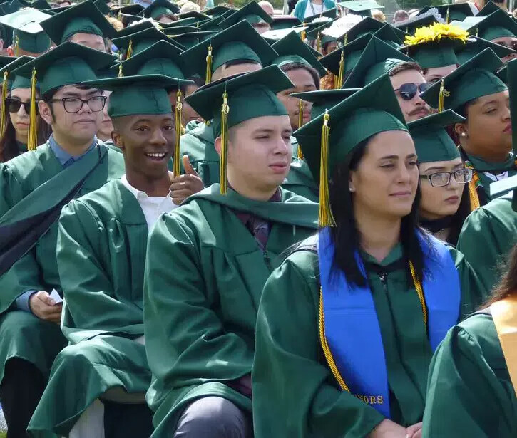 sea of seated graduates with one student giving thumbs up