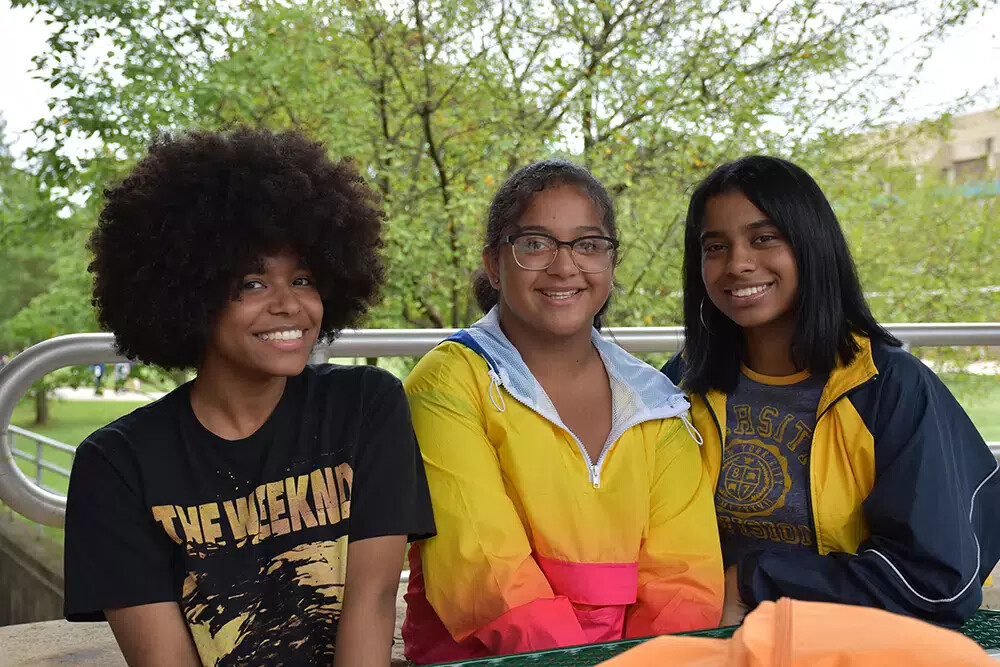 3 girls outside with girl in middle in gold shirt