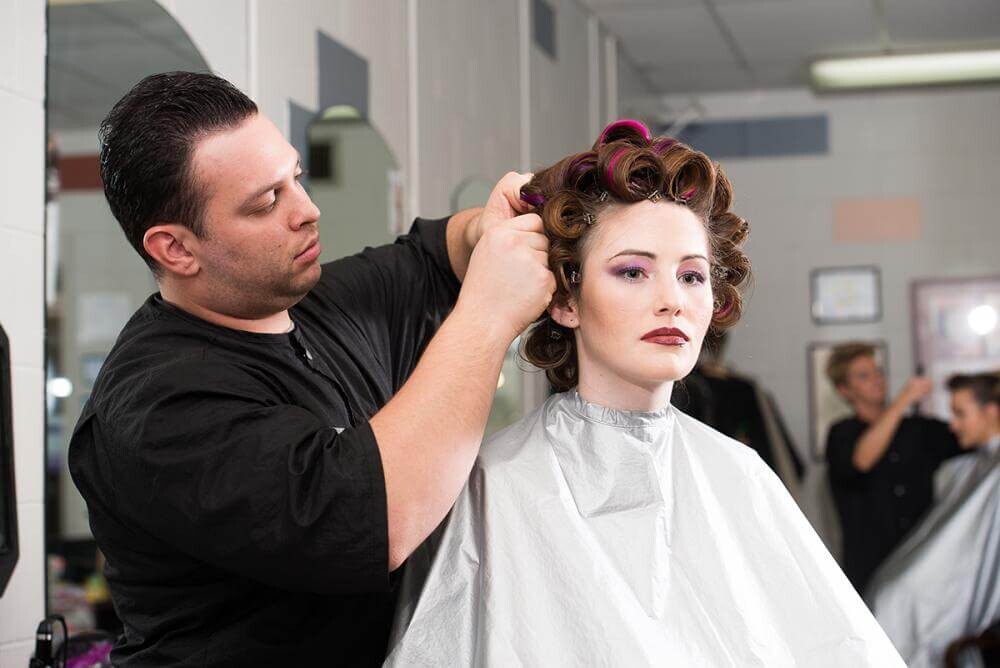 male cosmetology student working on model's hair