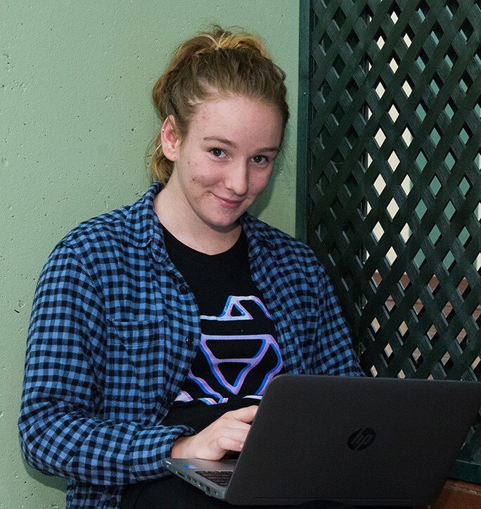 female student in ponytail, in blue shirt over tshirt holding laptop