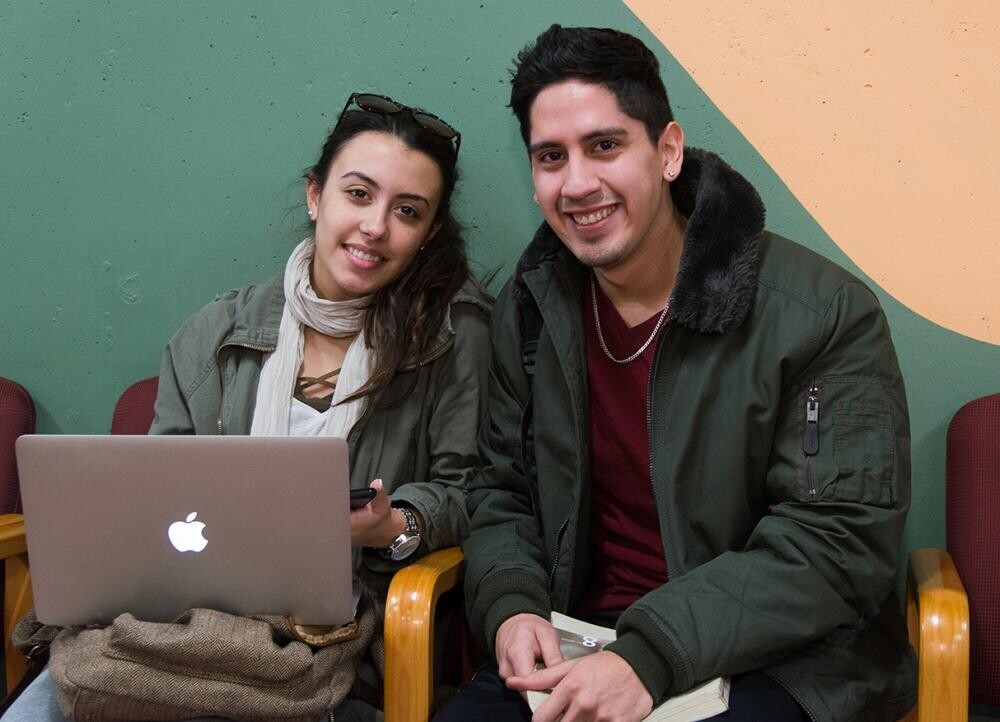 female student with laptop seated next to male student in jacket