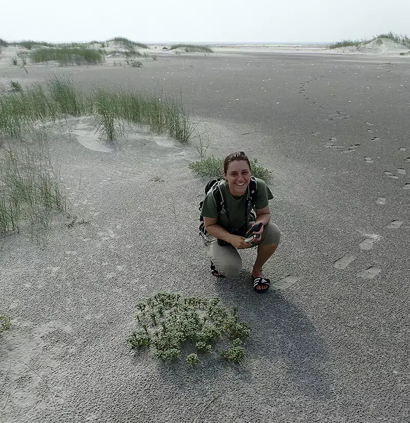 woman crouching down in sand with plants