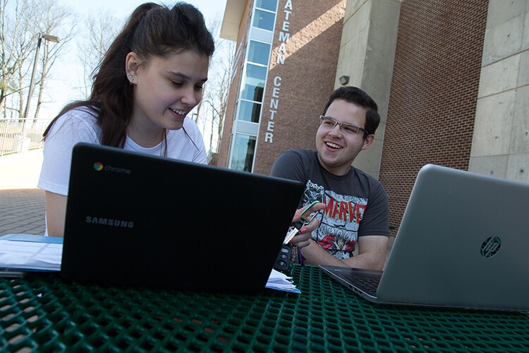 femal and male student outside with laptops