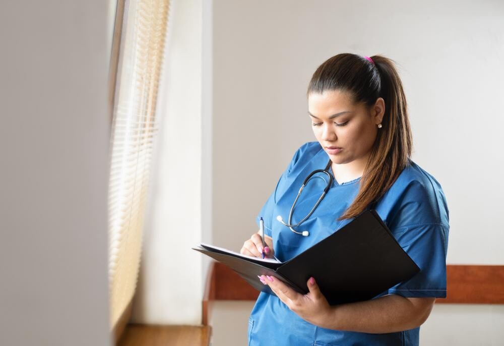 woman with ponytail in scrubs looking at folder