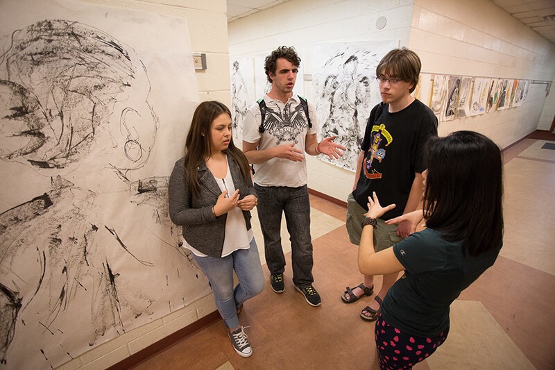 four students next to murals in arts building