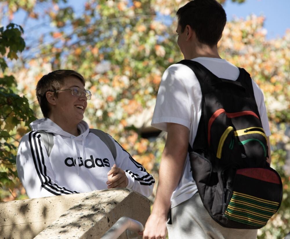 2 male students outside with one wearing backpack