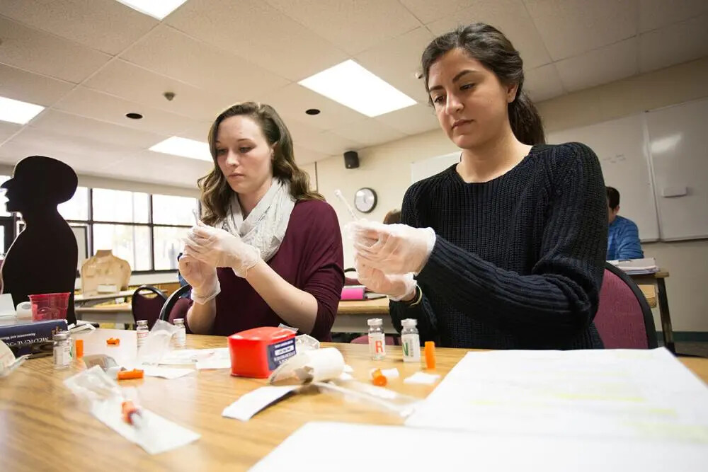 two female nursing students wearing gloves and working
