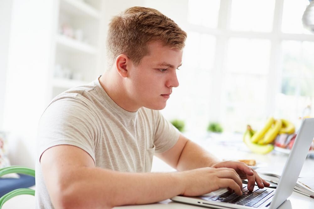 young man in white t-shirt working on laptop