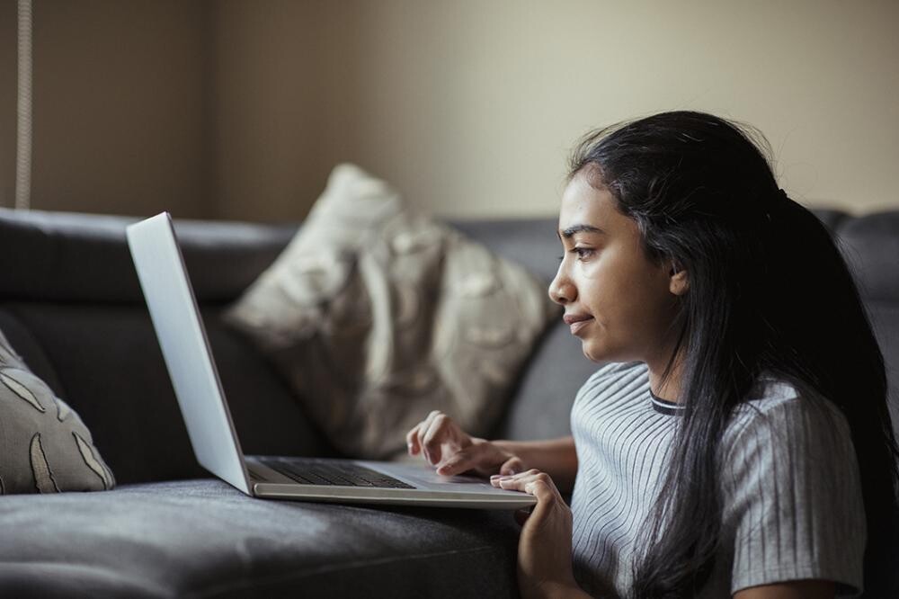 teen girl with pulled back hair and gray shirt on laptop at home