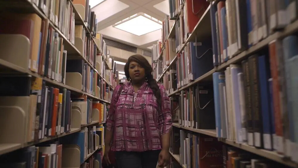 young woman walking between library shelves