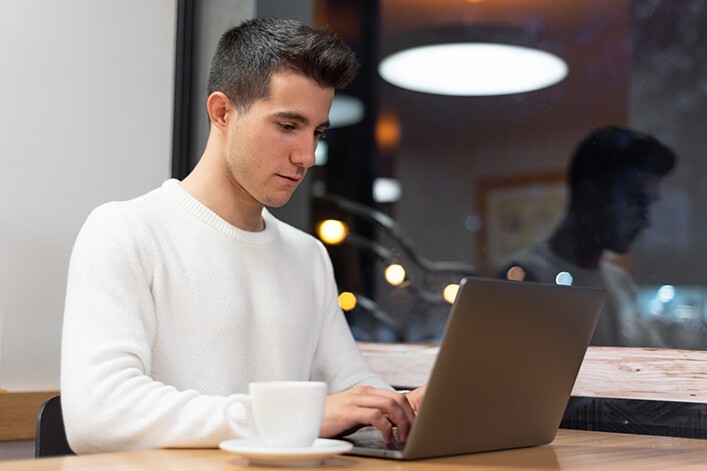 young man in white sweater on laptop with mirror
