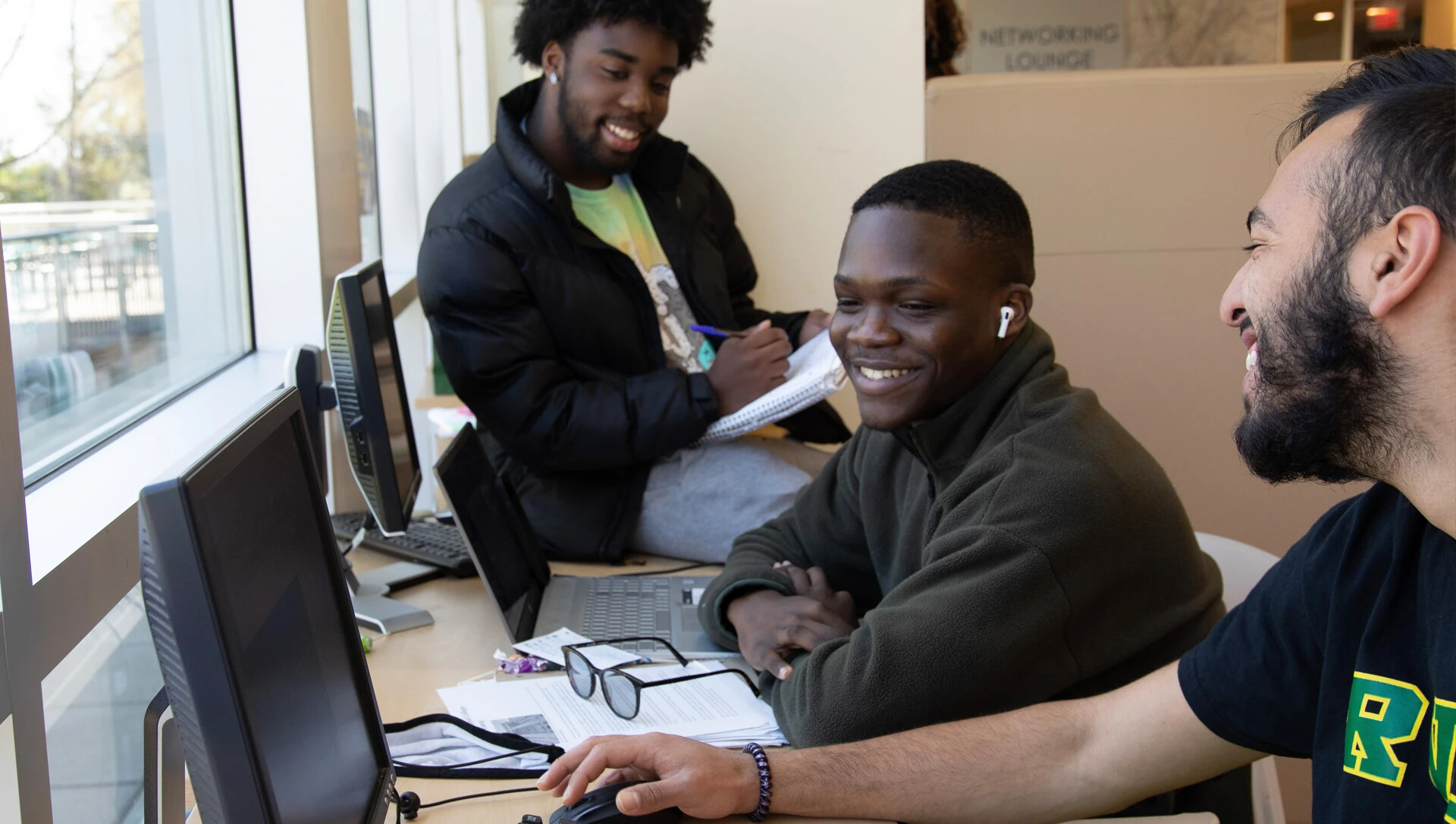 3 male students working at laptops, smiling and laughing