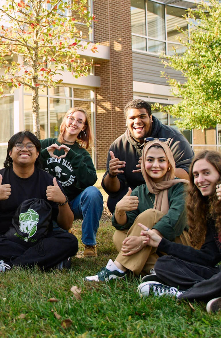 five college students sitting outside giving a thumbs up