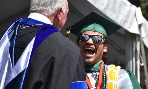 very happy graduate wearing sun glasses shaking President McDonoughs hand