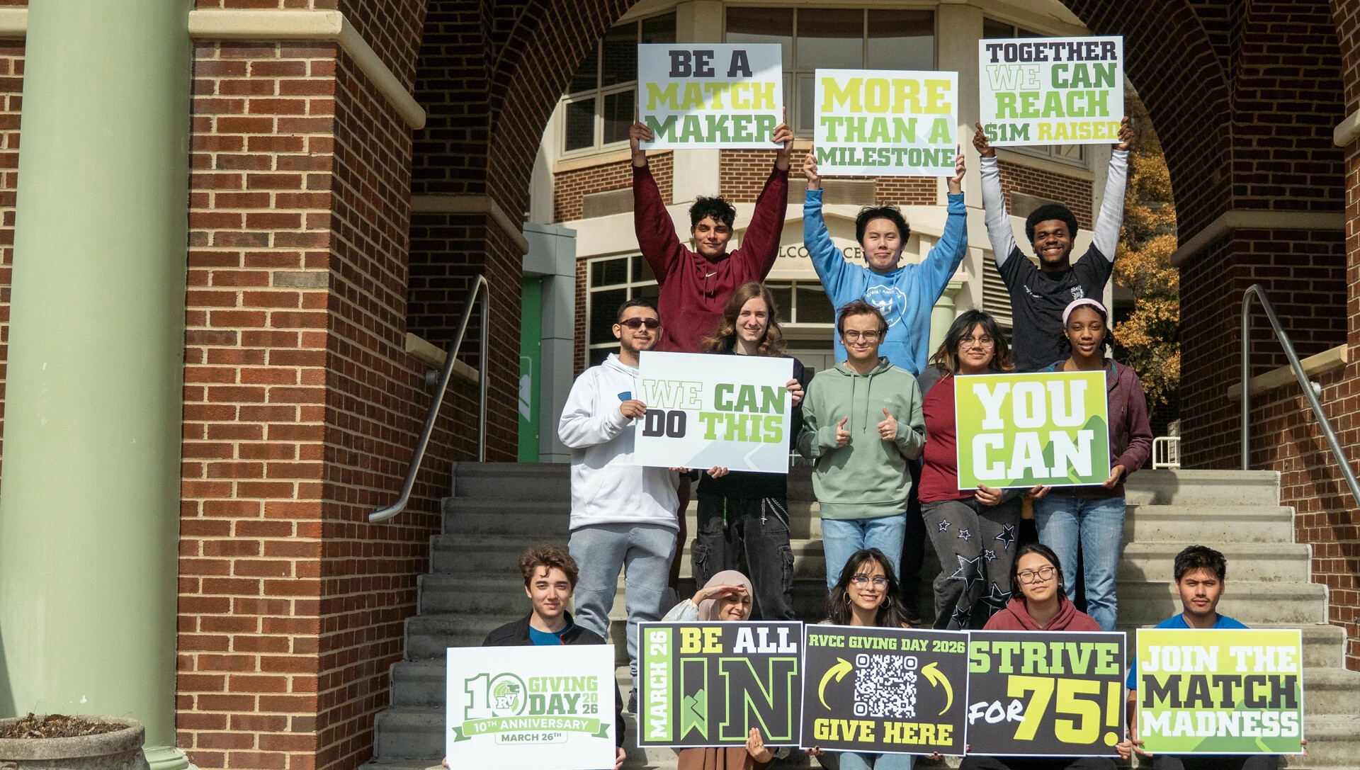 Group of student outside on the stairs, holding up signs promoting Giving Day donations