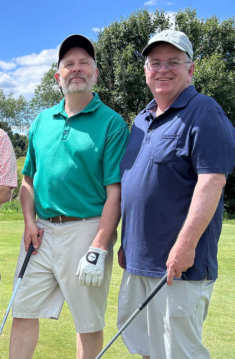 two men looking forward, smiling with golf clubs in hand