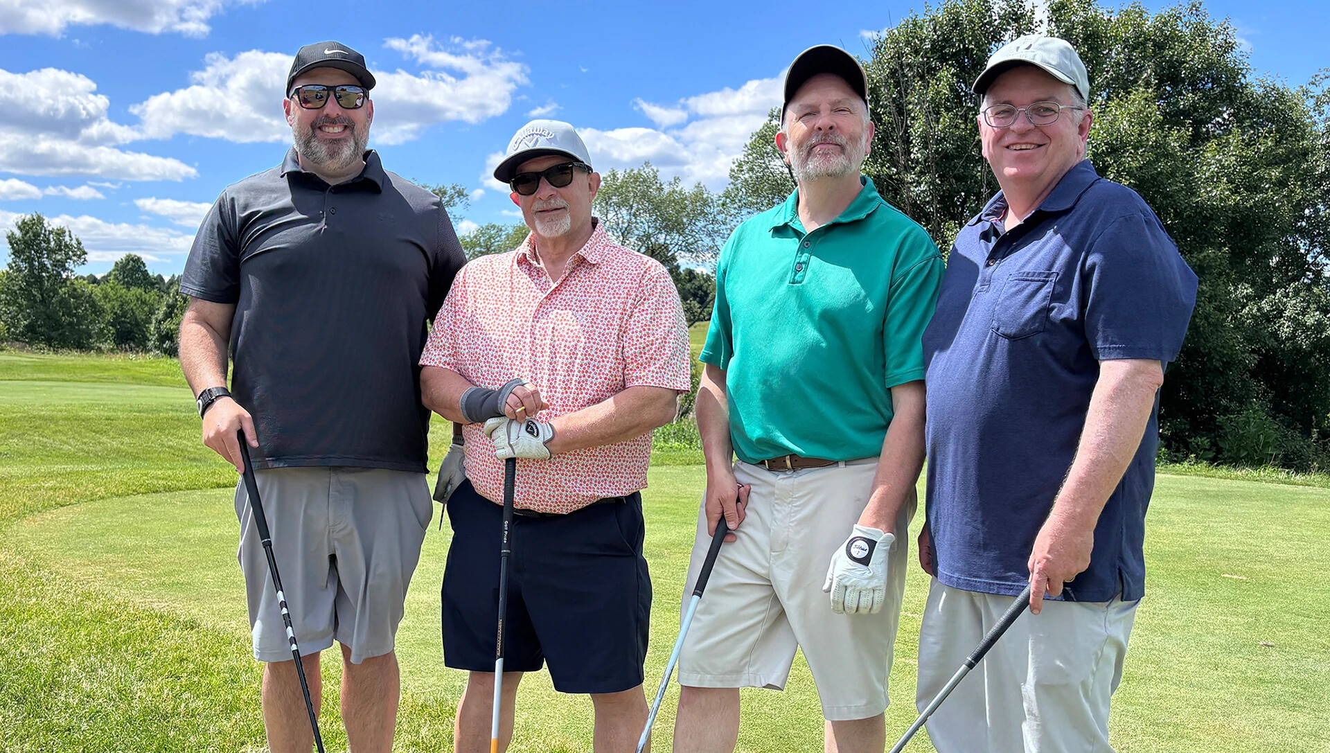 four men lined up looking at camera with gold clubs, hats and a single glove on each hand
