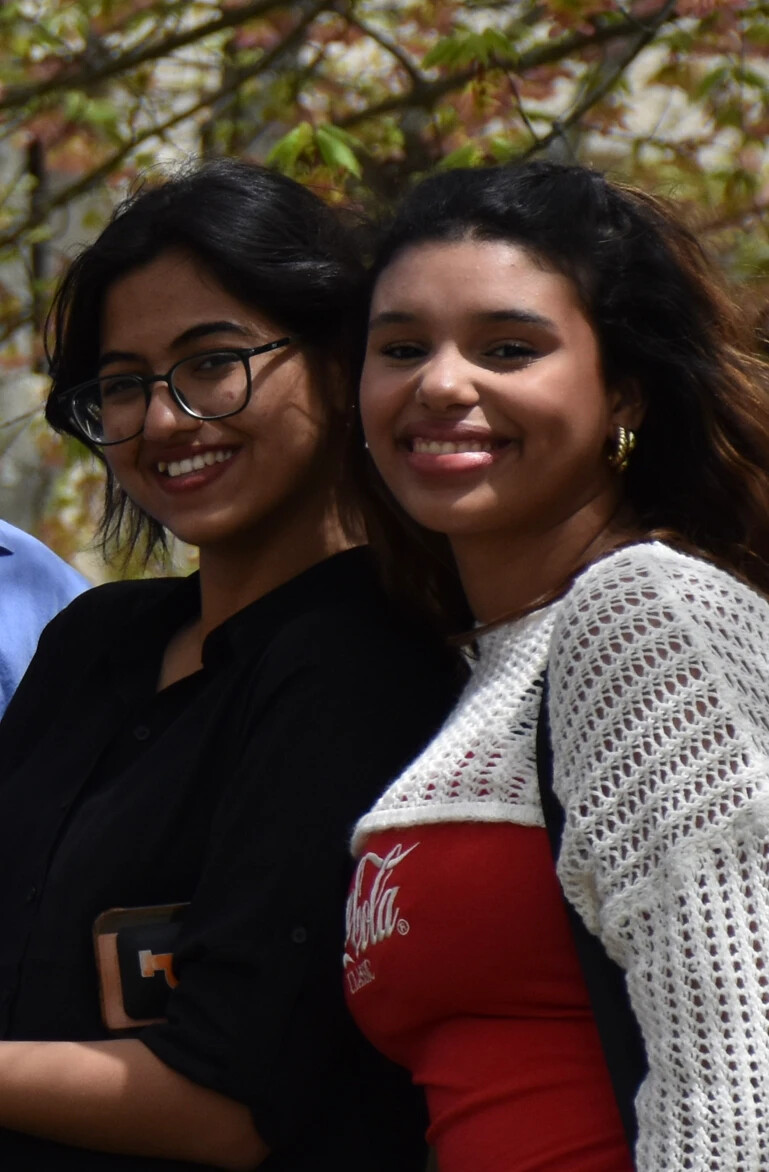 close up of two female students outside under the trees, lookin at camera smiling