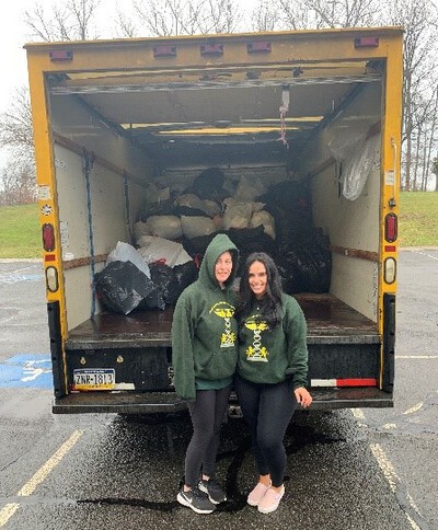 2 students in front of open truck with bags of clothes