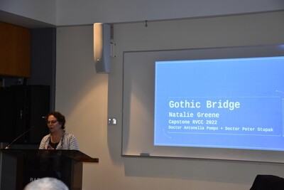 professor at podium with Gothic Bridge text on screen behind her