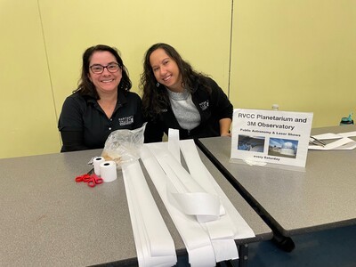 2 females behind table with long strips of paper