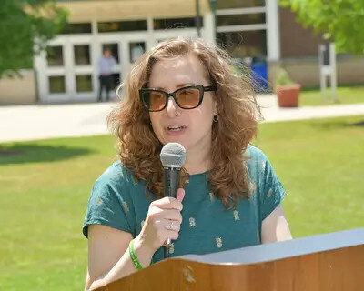 female speaker with curly hair and glasses speaking outside at podium