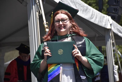 RVCC graduate posing with their degree and wearing a rainbow graduation stole.