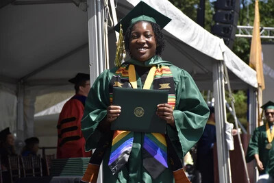 RVCC graduate posing with their degree and wearing a rainbow graduation stole.