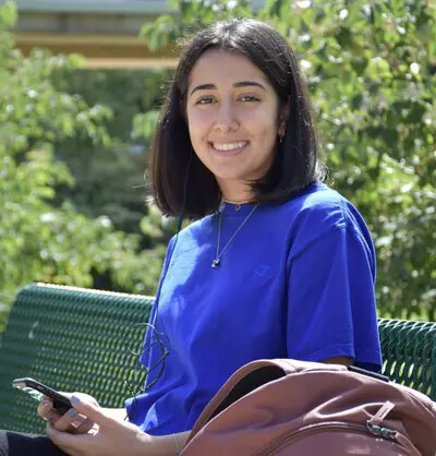 girl with dark brown hair outside on bench wearing bright blue shirt