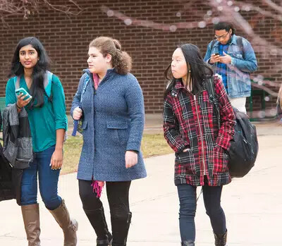 3 girls in coats walking outside with male student on phone