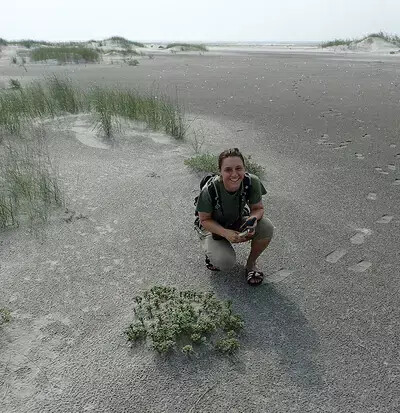 woman crouching down in sand with plants