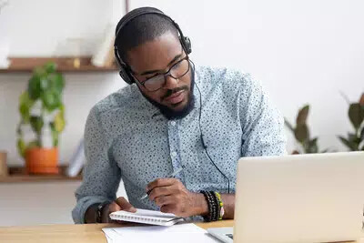 man wearing headphones taking notes and looking at tablet
