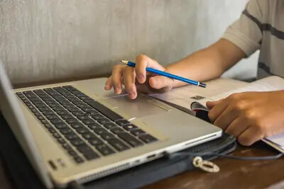 student holding pencil working on laptop