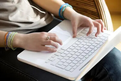 girl's hands with bracelets working on laptop