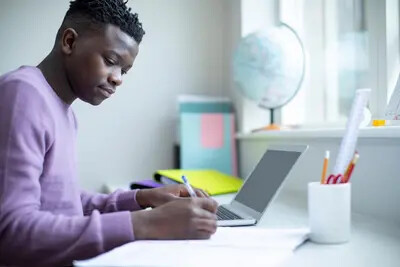 young man in purple sweater working on laptop and writing